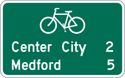 Two line bicycle distance guide sign showing mileage to multiple destinations