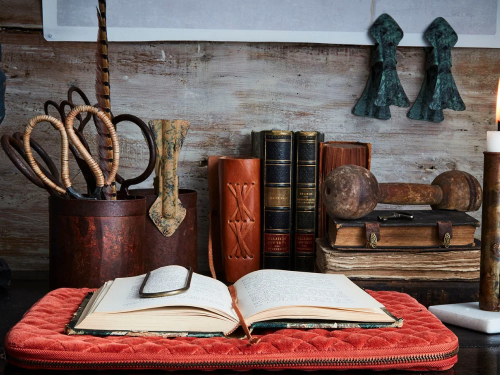 A warm, aspirational interior still-life featuring a large terracotta urn with dried branches, a ceramic vase, and a lit candle in a sunlit room.
