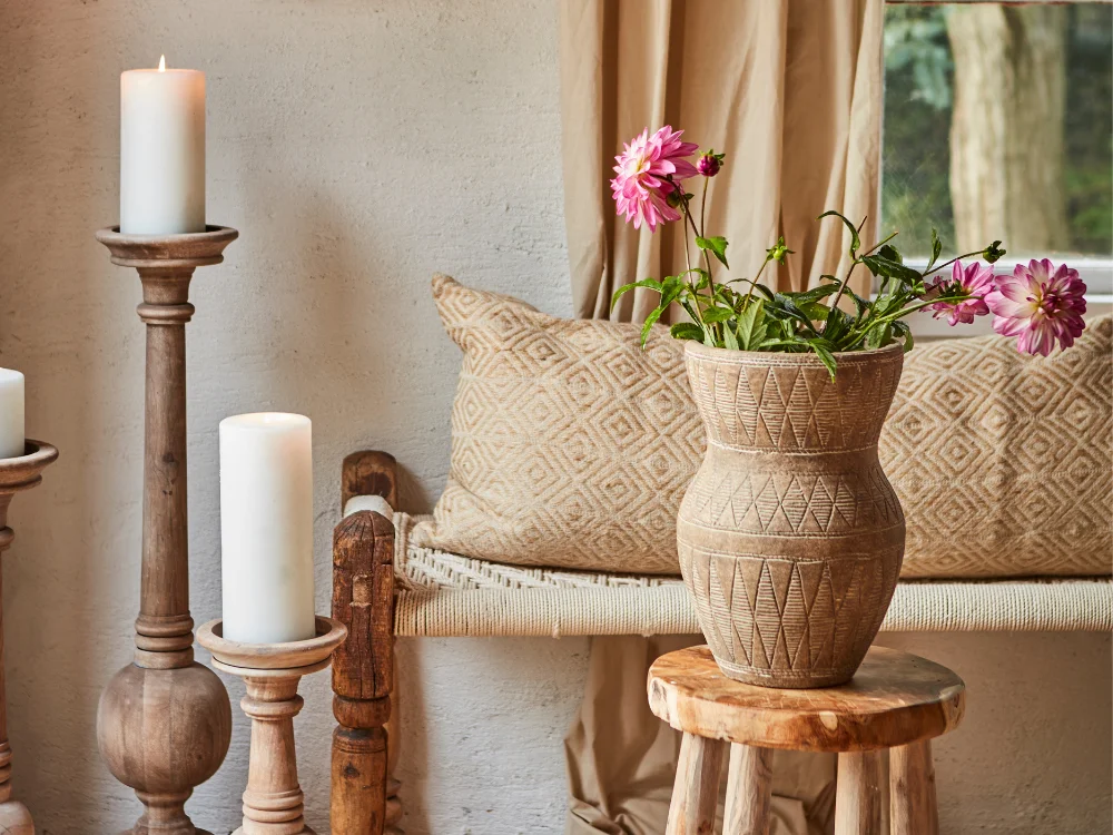 A serene still-life of minimalist home decor featuring a ceramic urn, a textured linen cloth, and a candle on a natural wood surface in soft sunlight.