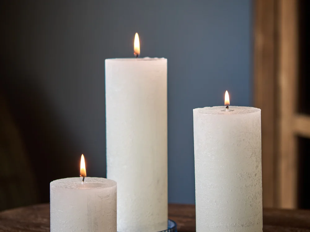 A serene, close-up shot of a high-quality white pillar candle burning evenly on a stone base, featuring a steady flame and a perfectly symmetrical wax pool in a warm, aspirational 
