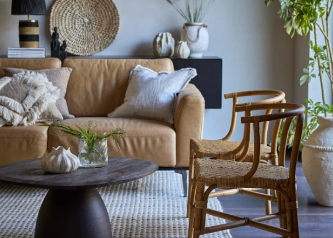 A serene and warm interior still life featuring artisanal ceramic vessels, a black bowl, and linen textiles on a wooden surface, bathed in soft natural light.