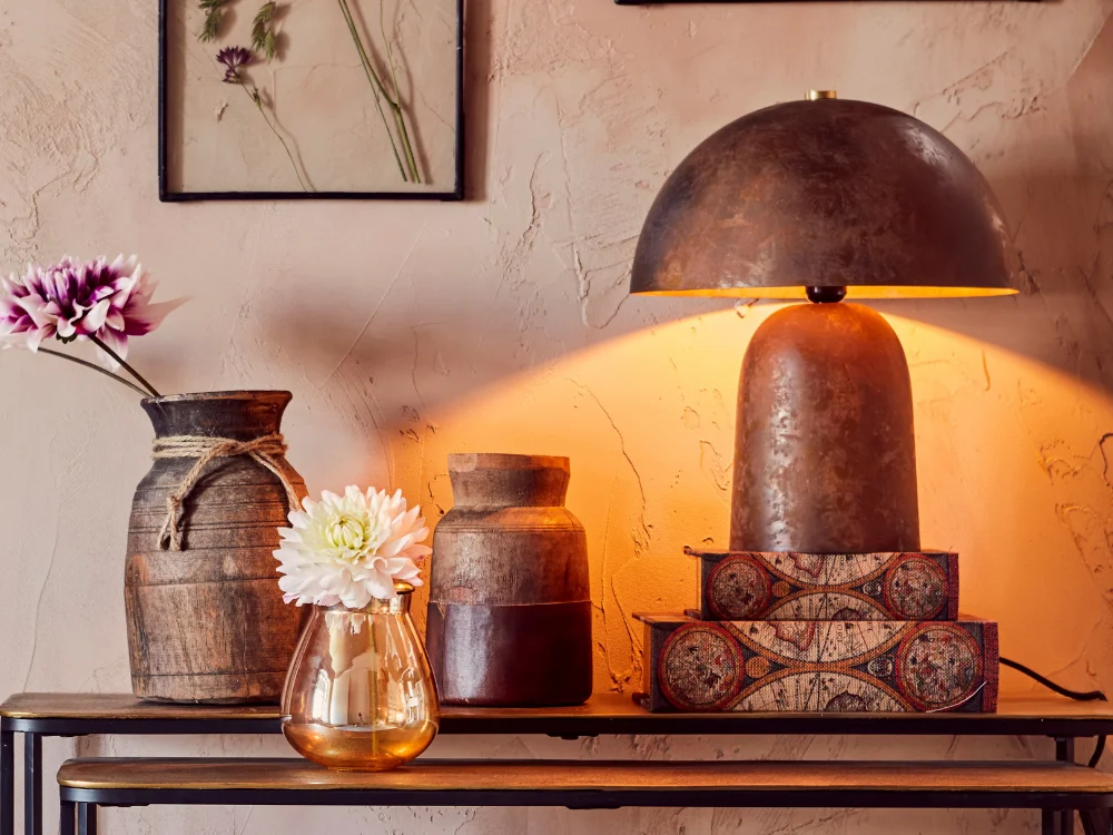 A serene and warm-toned still life of a bedroom bedside table featuring a glowing handmade candle, a soft lamp, and a glass vase, creating a relaxing atmosphere.