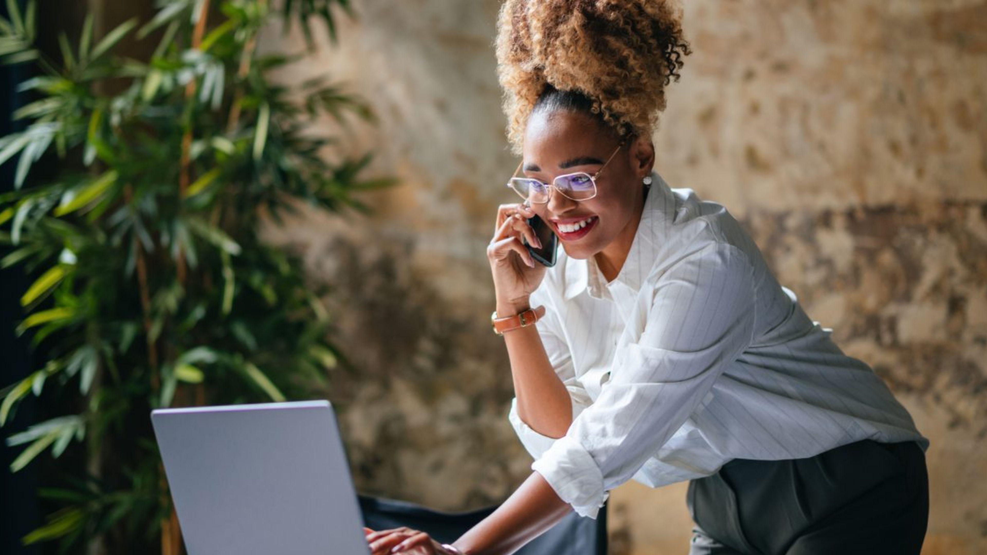 woman looking at phone with laptop on desk 