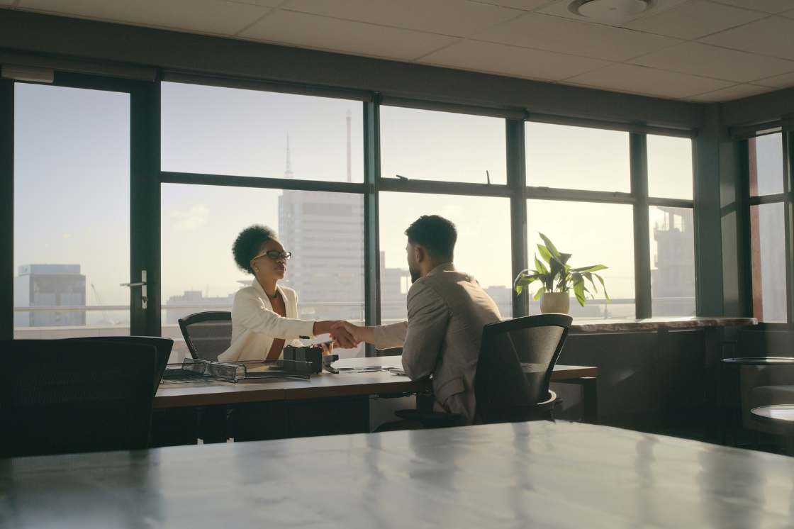 two people talking over a desk, shaking hands
