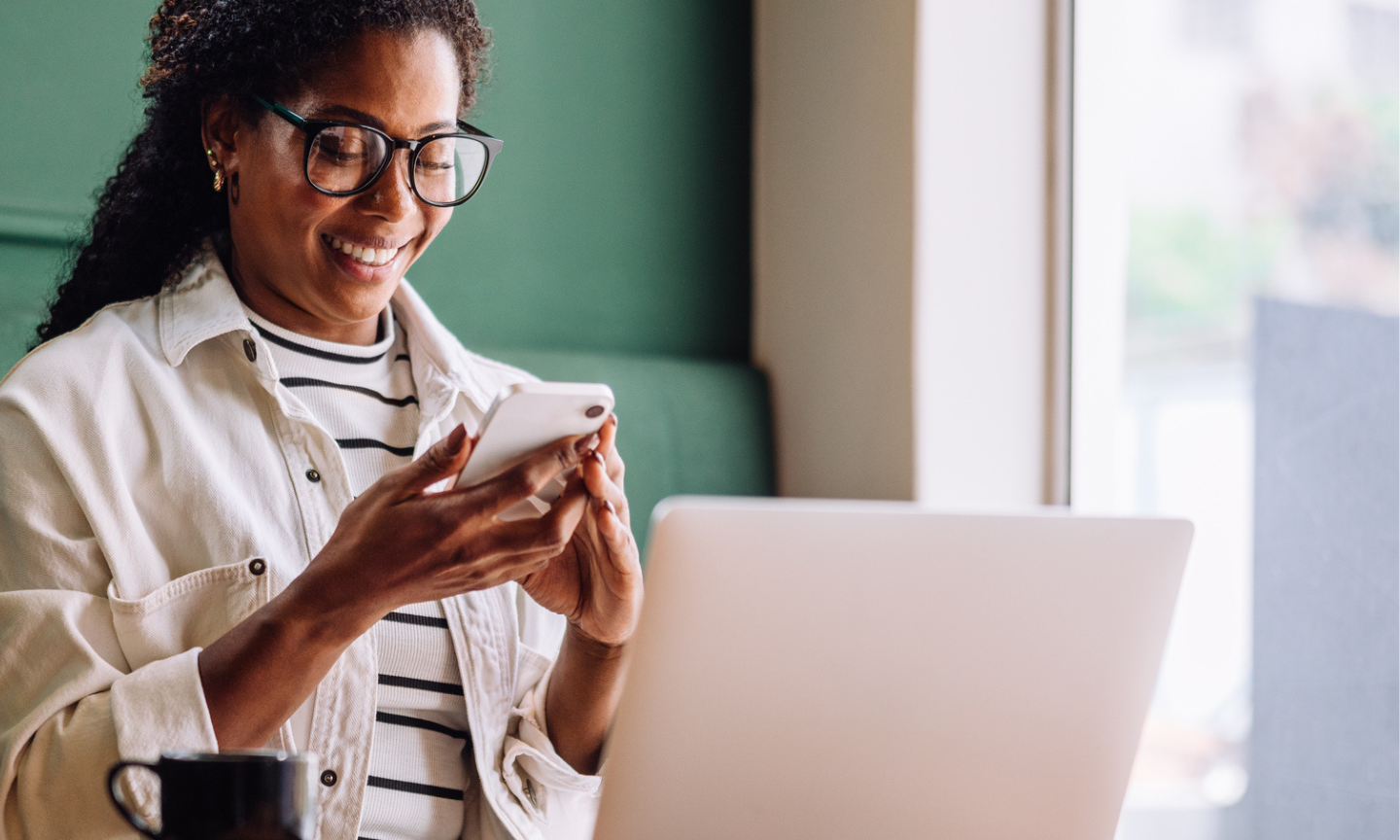 woman looking at phone with laptop on desk 