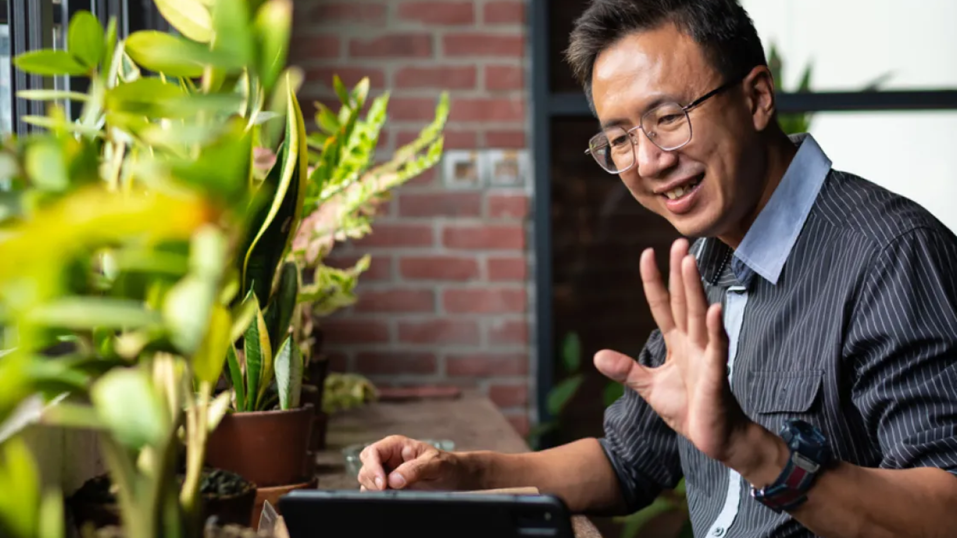 man waving at laptop screen, on video call