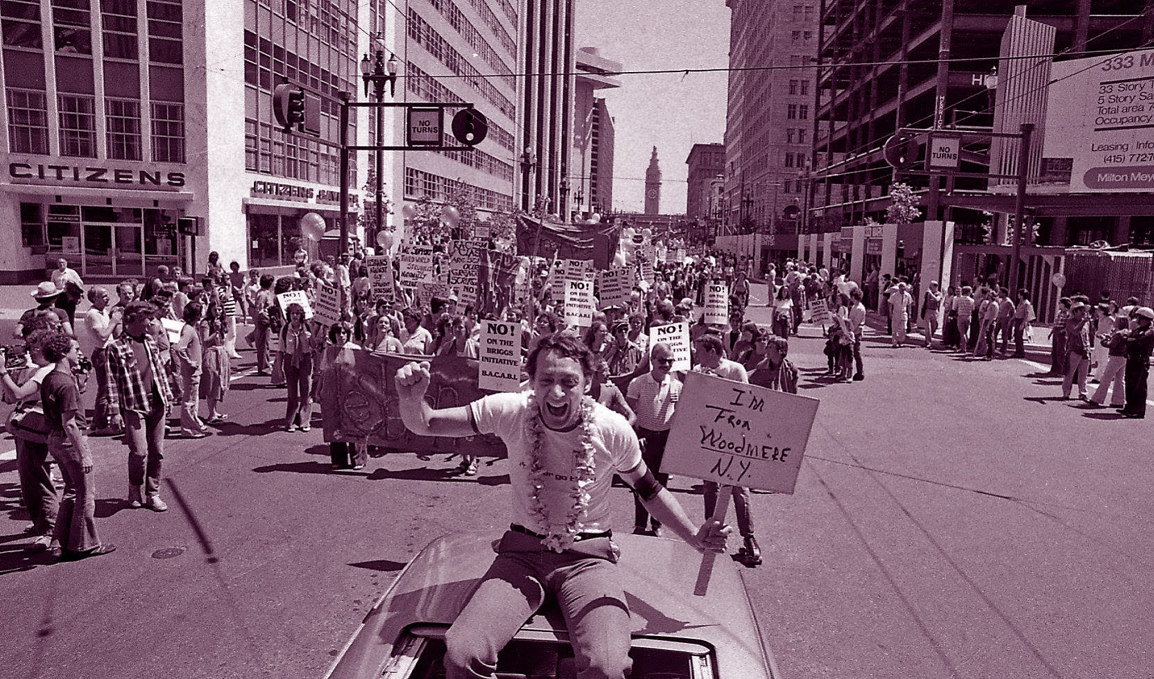 Harvey Milk riding in a car, holding a sign that reads im from woodshire new york, the car a part of the sf pride parade