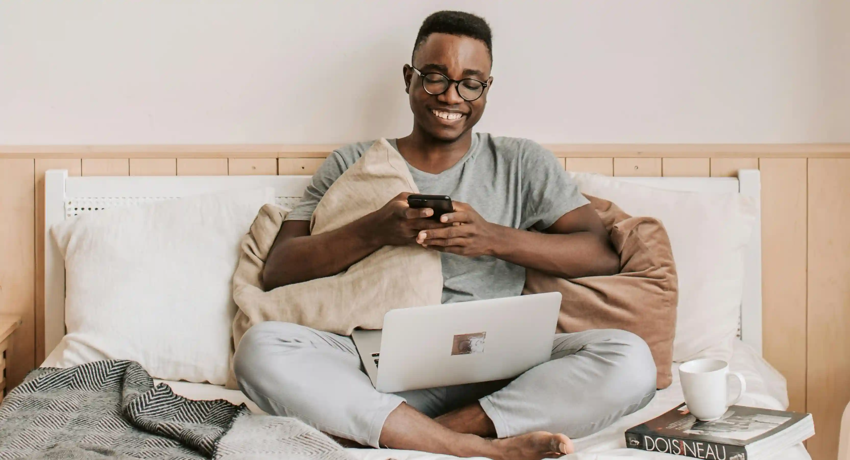 A man smiling at his phone while sitting on his bed