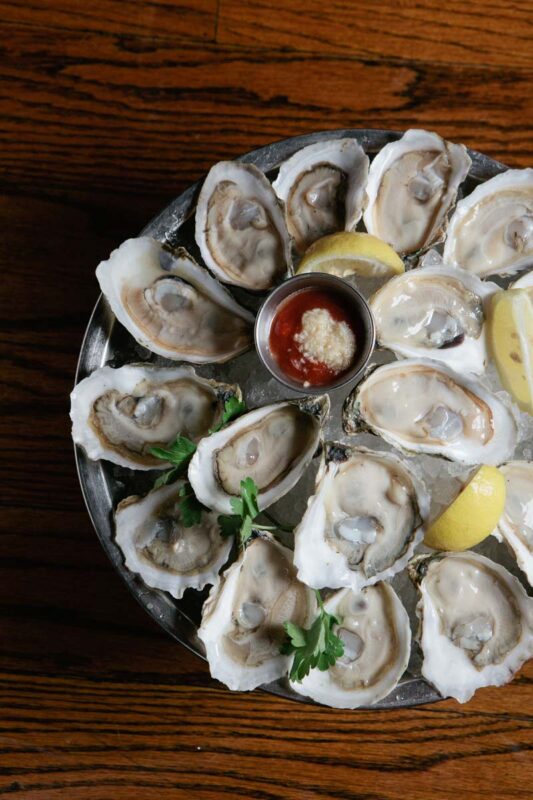overhead photo of a tray of oysters with lemons and cocktail sauce on crushed ice