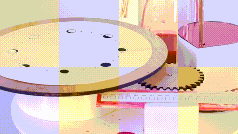 A close-up of a circular chart printed on paper, surrounded by a kinetic sculpture with gears and tubes. Red fluid drips onto a calendar-style display below, visualizing menstrual cycles through a mechanized and analog interaction of ink and motion.