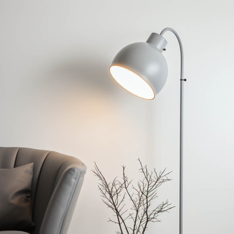 Moderne Stehlampe mit runder Schirm, grauer Farbton, neben einem eleganten Sessel und einem minimalistischen Zweig in einer stilvollen Inneneinrichtung.