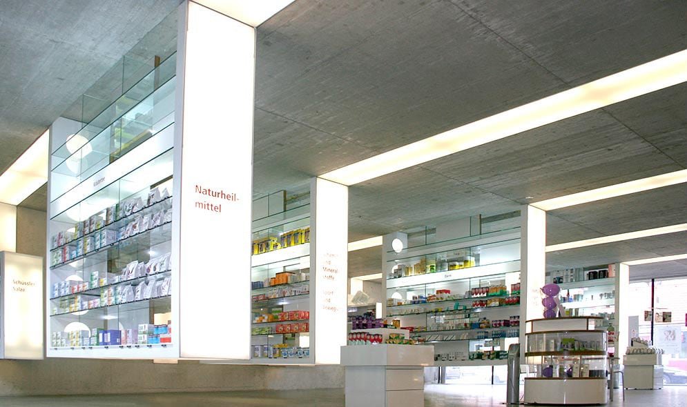 Moderne Apotheke mit offenen Regalen, die eine Vielzahl von Gesundheits- und Pflegeprodukten präsentieren. Helle Beleuchtung und minimalistische Architektur schaffen eine einladende Atmosphäre.