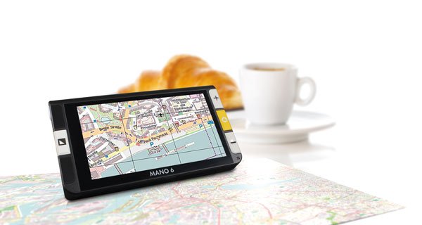 Elektronische Lupe MANO 6 zeigt eine vergrößerte Stadtkarte, im Hintergrund Kaffee und Croissants auf einem Tisch