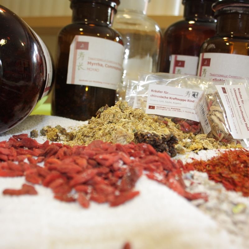 Eine Sammlung von Kräutern und Gewürzen auf einem Tisch, darunter Myrrhe und andere pflanzliche Zutaten, in Gläsern aufgestellt. Die Gewürze sind in verschiedenen Formen und Farben angeordnet, was auf eine Nutzung in der traditionellen oder alternativen Medizin hindeutet.