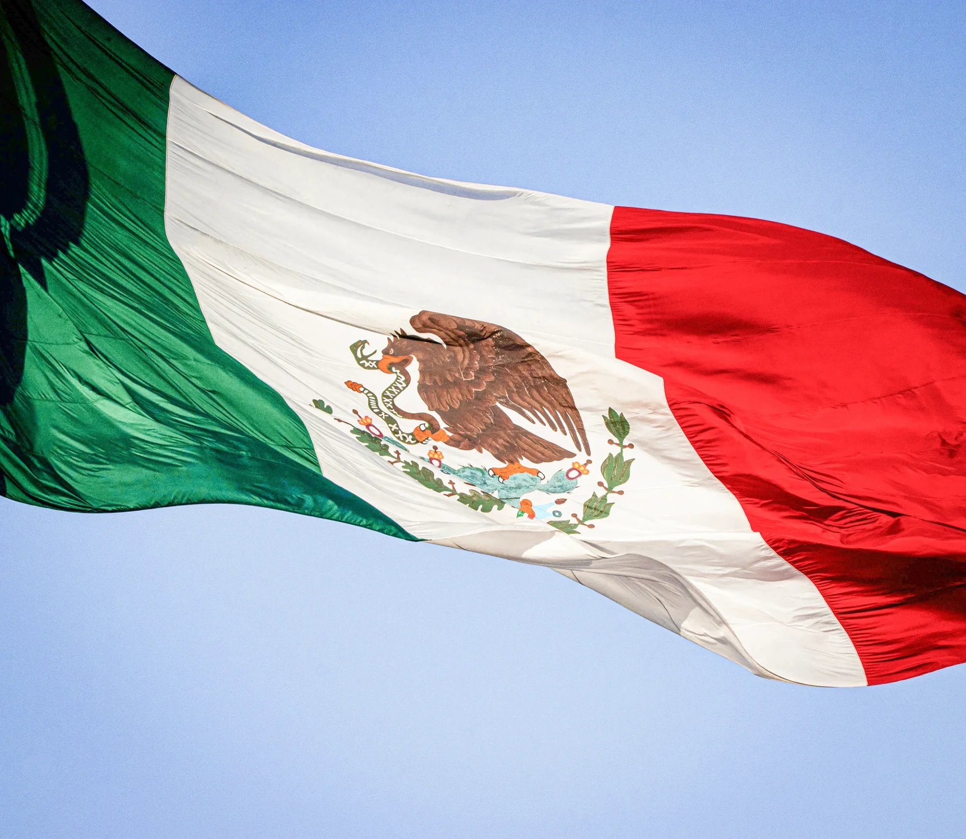 Flag of Mexico, consisting of three vertical stripes in green, white, and red, with the national coat of arms in the center, depicting an eagle holding a snake.
