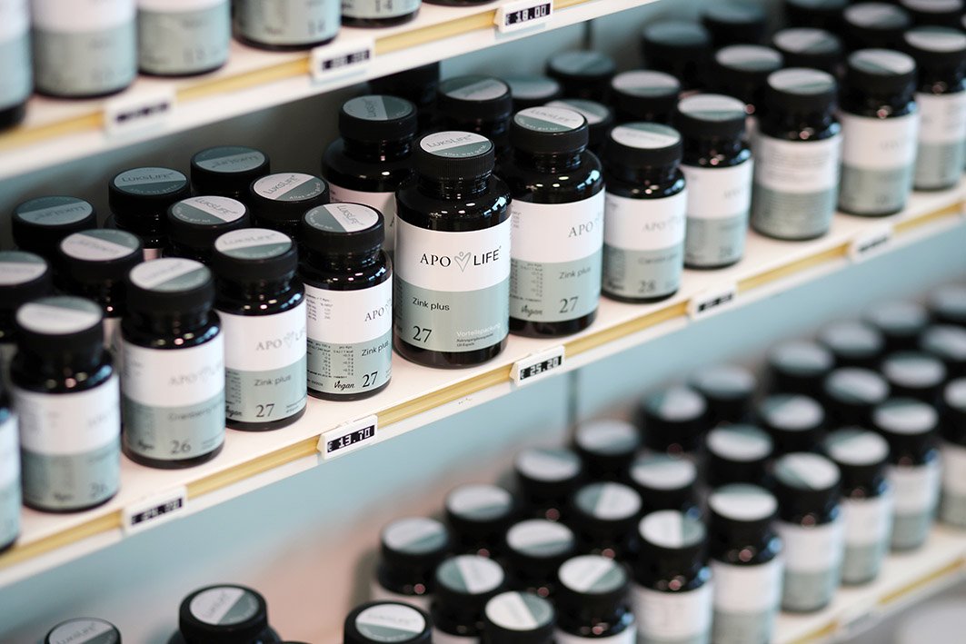 Regal mit verschiedenen Nahrungsergänzungsmitteln von Apo Life, die in dunklen Flaschen aufgereiht sind. Jedes Produkt hat ein elegantes Design mit klaren Etiketten, die die Produktnummern anzeigen. Ideal für eine gesunde Lebensweise.