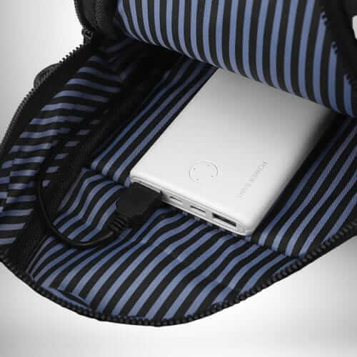 Intérieur d'un sac banane homme luxe noir ouvert, contenant une batterie externe blanche branchée avec un câble noir. Le tissu intérieur est rayé noir et bleu clair.