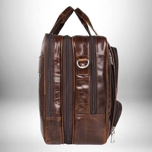 Une vue latérale d'une sacoche médecin de couleur brun foncé. Elle est faite de cuir ou d'un matériau similaire et présente plusieurs poches et compartiments avec des fermetures éclair et des détails en métal. Le sac a une poignée en cuir et semble robuste et durable.