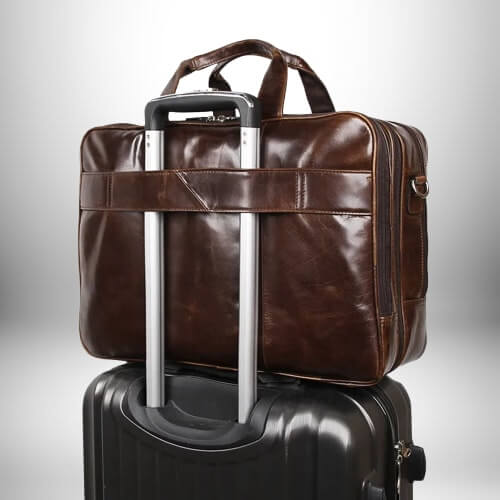 Une sacoche medecin en cuir marron est posée sur une valise noire, les poignées de la valise sont insérées dans la sangle prévue sur la sacoche.