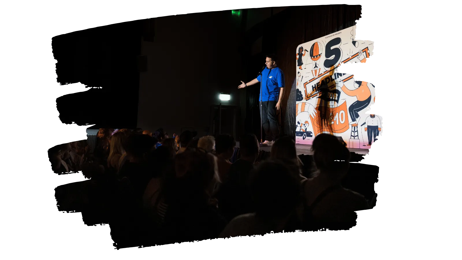 A comedian on stage telling jokes to an audience shrouded in darkness