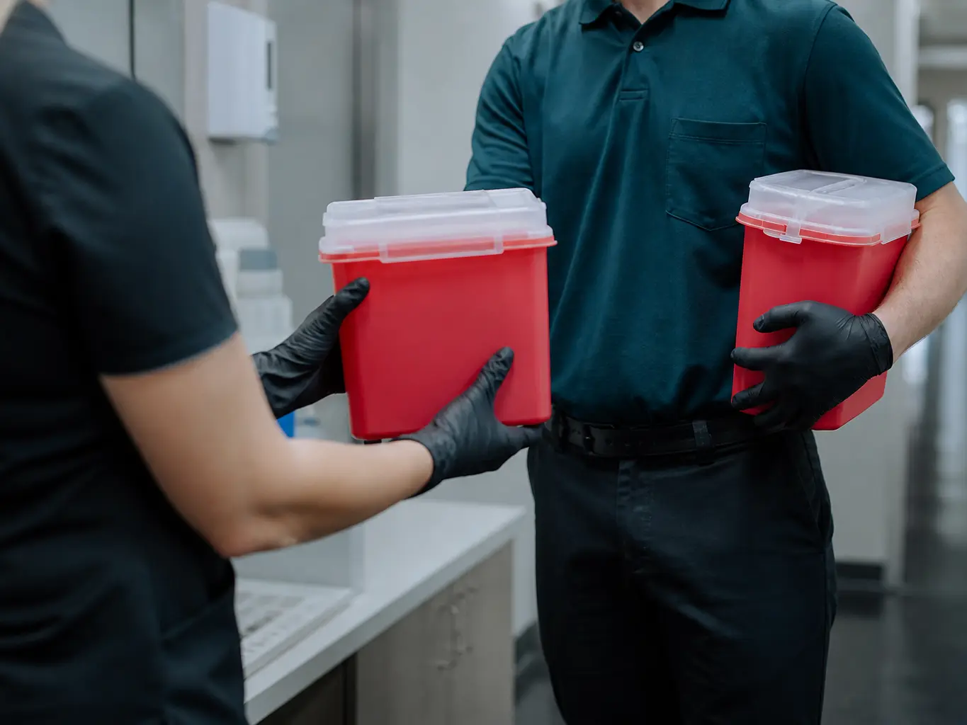 Technician handing a clean sharps container to clinic staff while carrying away the sealed full one