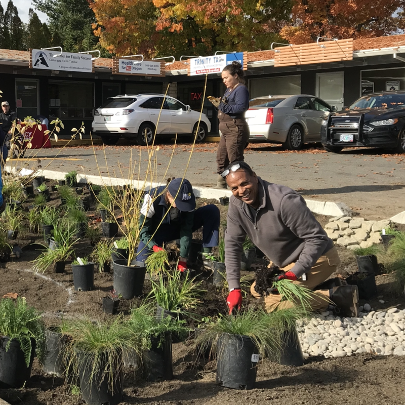Photograph of two people gardening in front of a low-rise commercial center