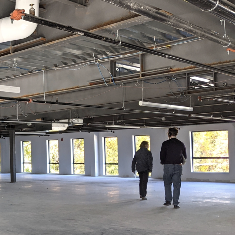 Two people walk in an open, empty industrial space with concrete floors.