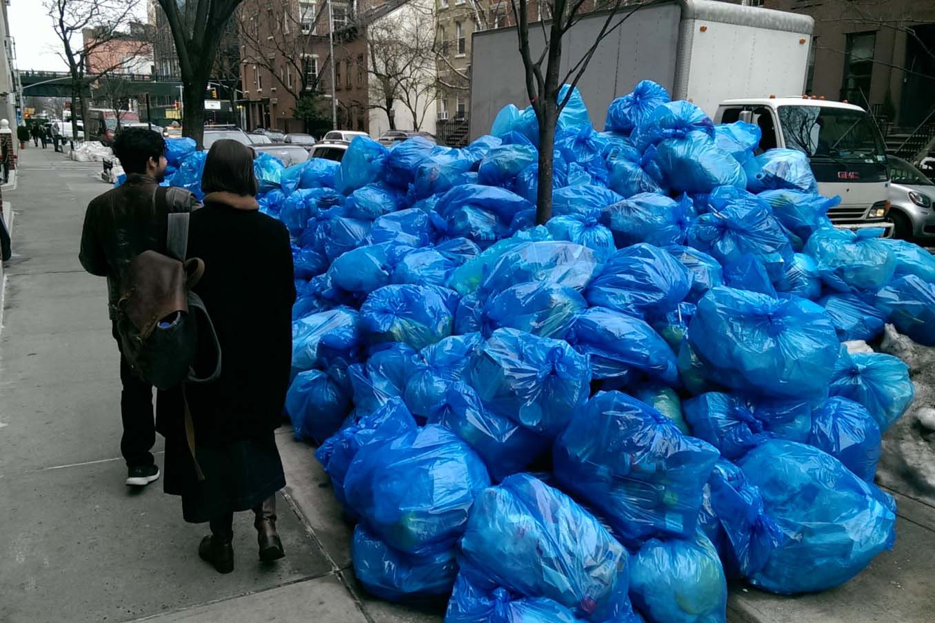 Passersby look at piles of garbage on a NYC sidewalk