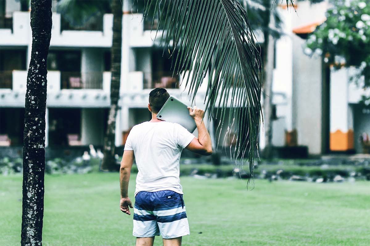 Young freelancer man with laptop in the green tropical park of Bali island, Indonesia.
