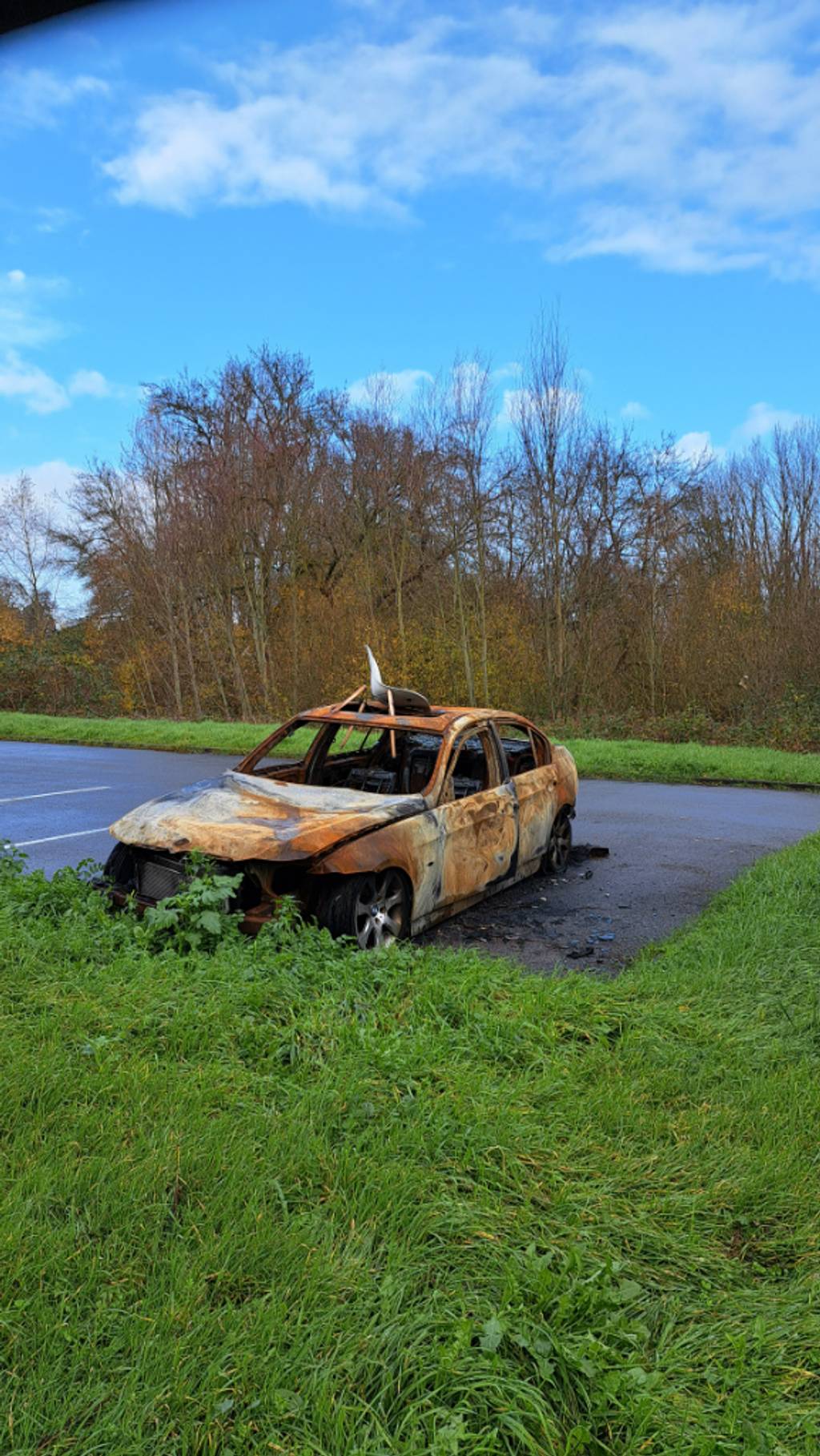 Voiture incendiée abandonnée sur parking.