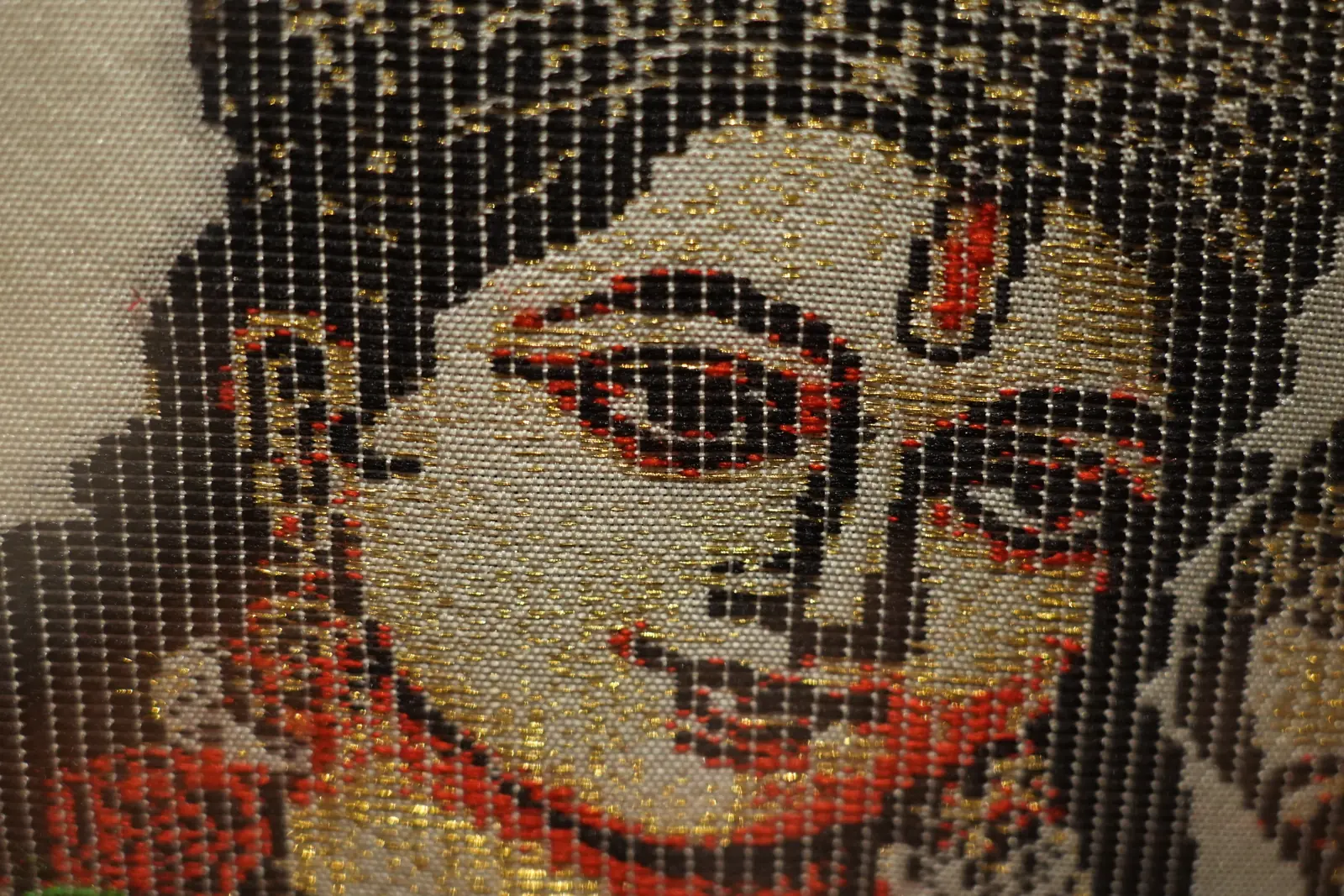 Close-up of a face woven in silk with gold zari, showing fine detail around the eye