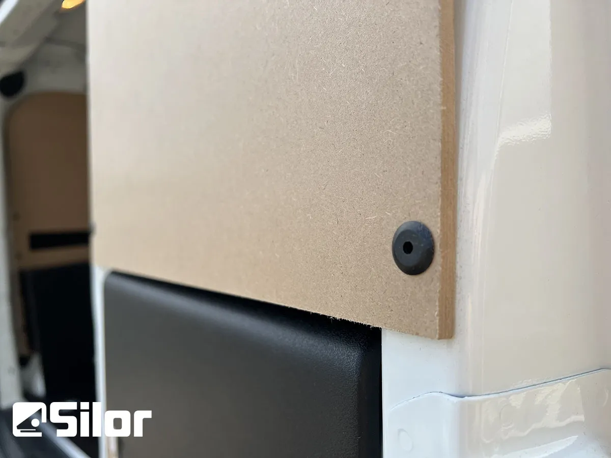 Un pannello di legno chiaro fissato al rivestimento interno di un furgone bianco con un fermo nero.