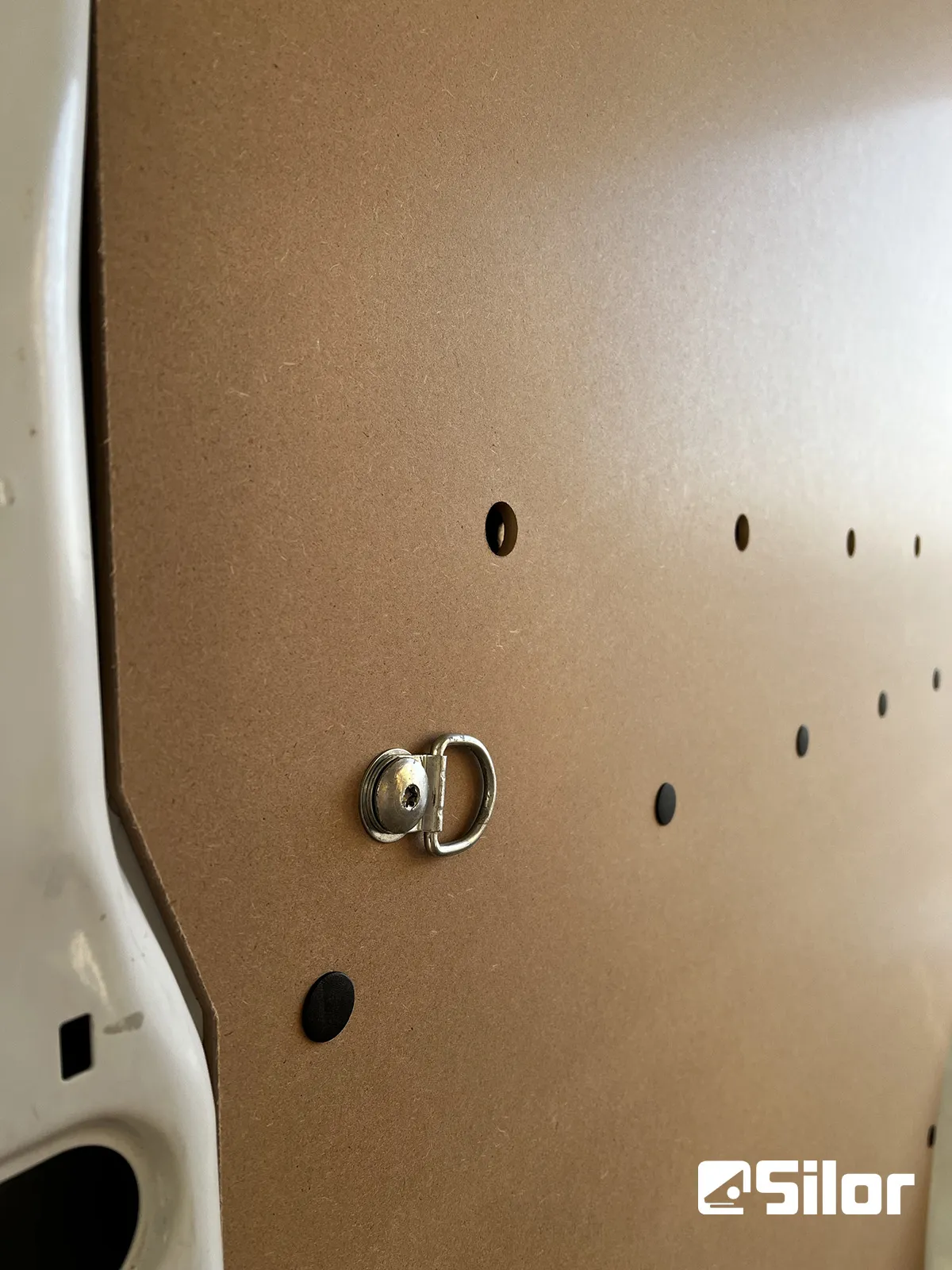 Una parete di compensato con un anello a D e piccoli fori.
