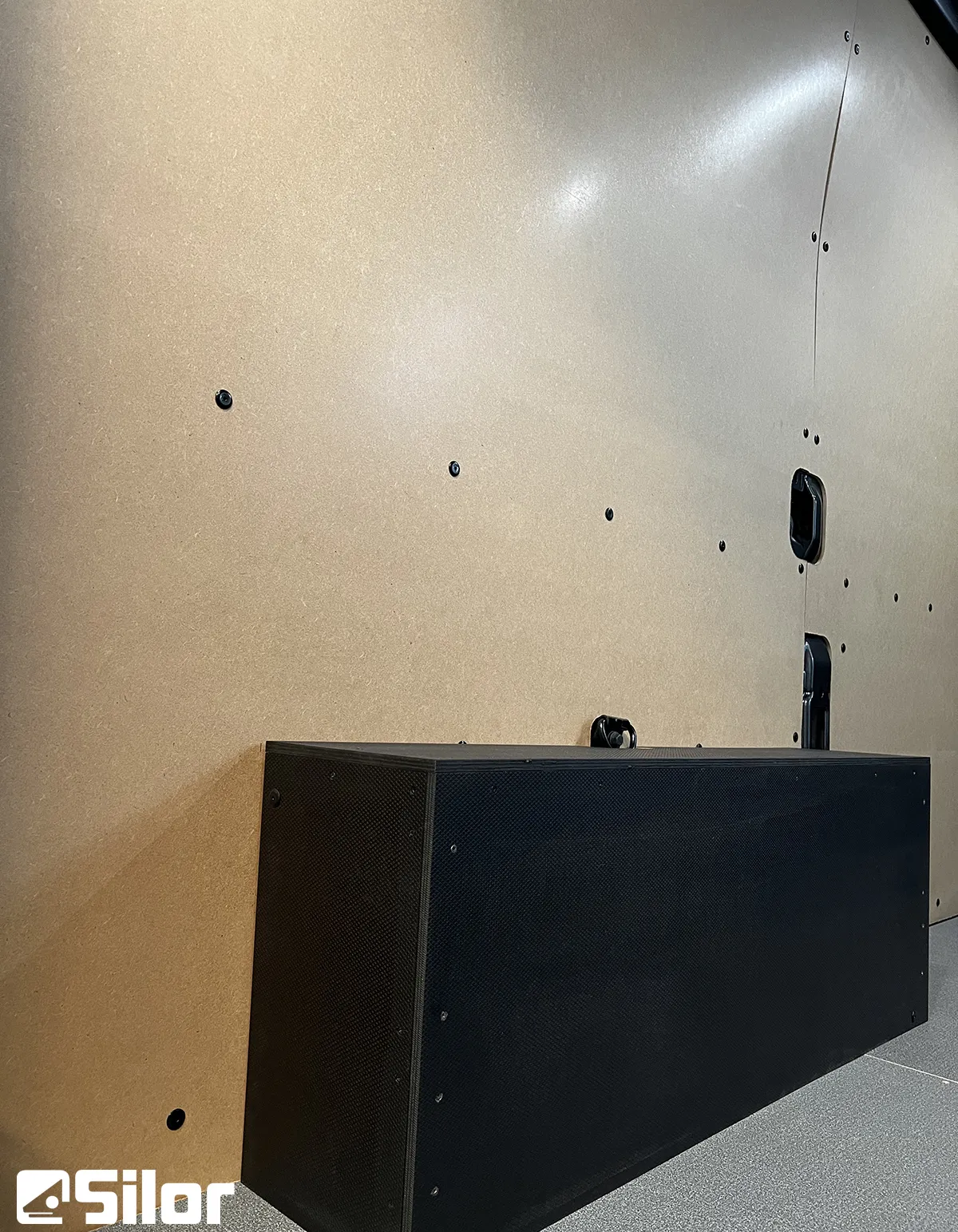 Interni di un furgone con pareti in legno chiaro e un contenitore nero sul pavimento.