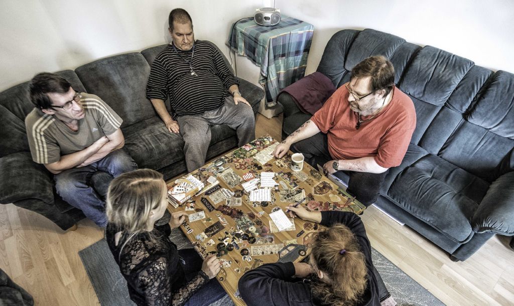 Joukko ihmisiä pelaamasaa Yatzya sohvapöydän ympärillä.