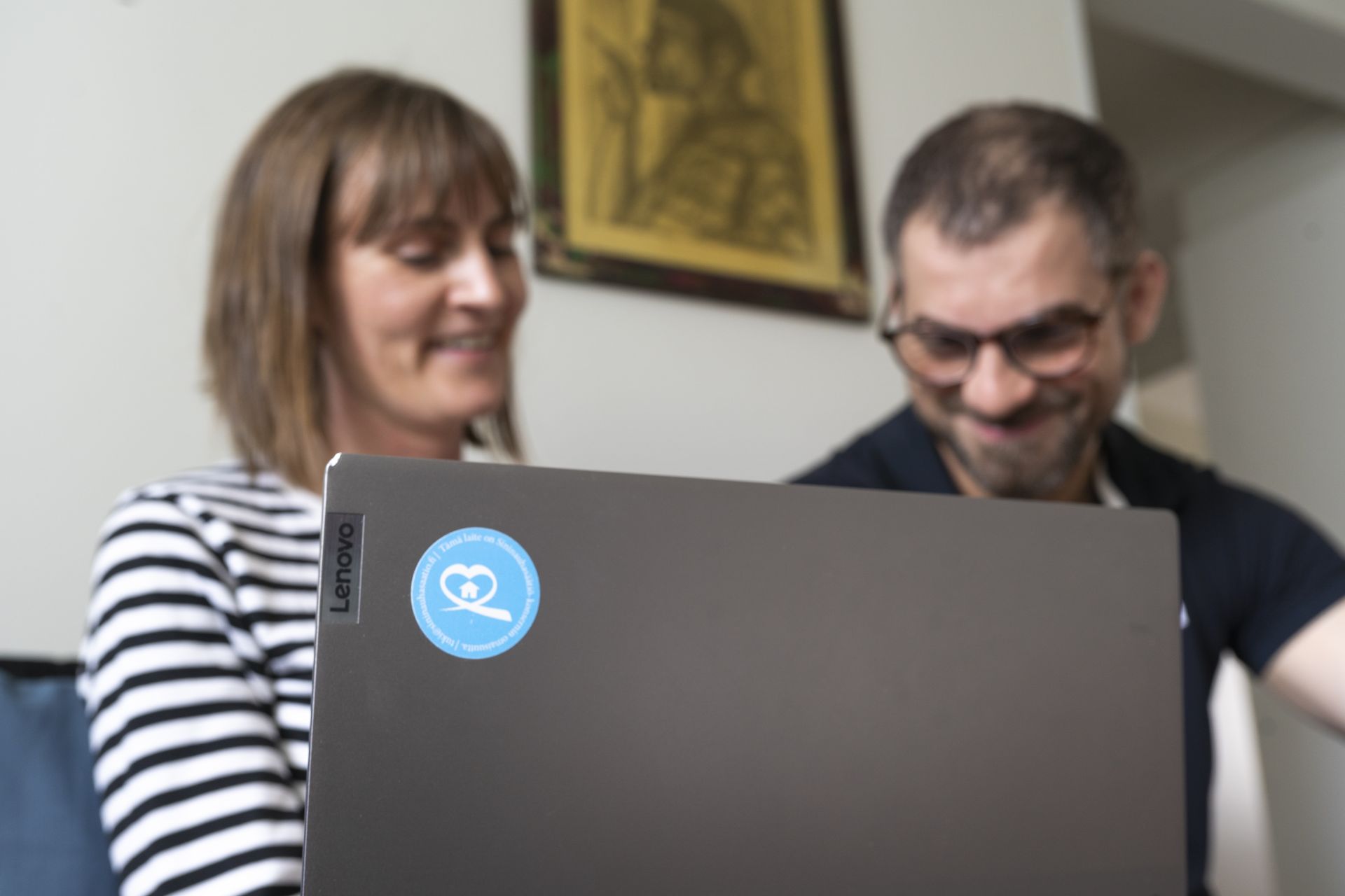 Kaksi ihmistä keskustelee kannettavan tietokoneen ääressä, Sininauhasäätiön logo ja valokuva.