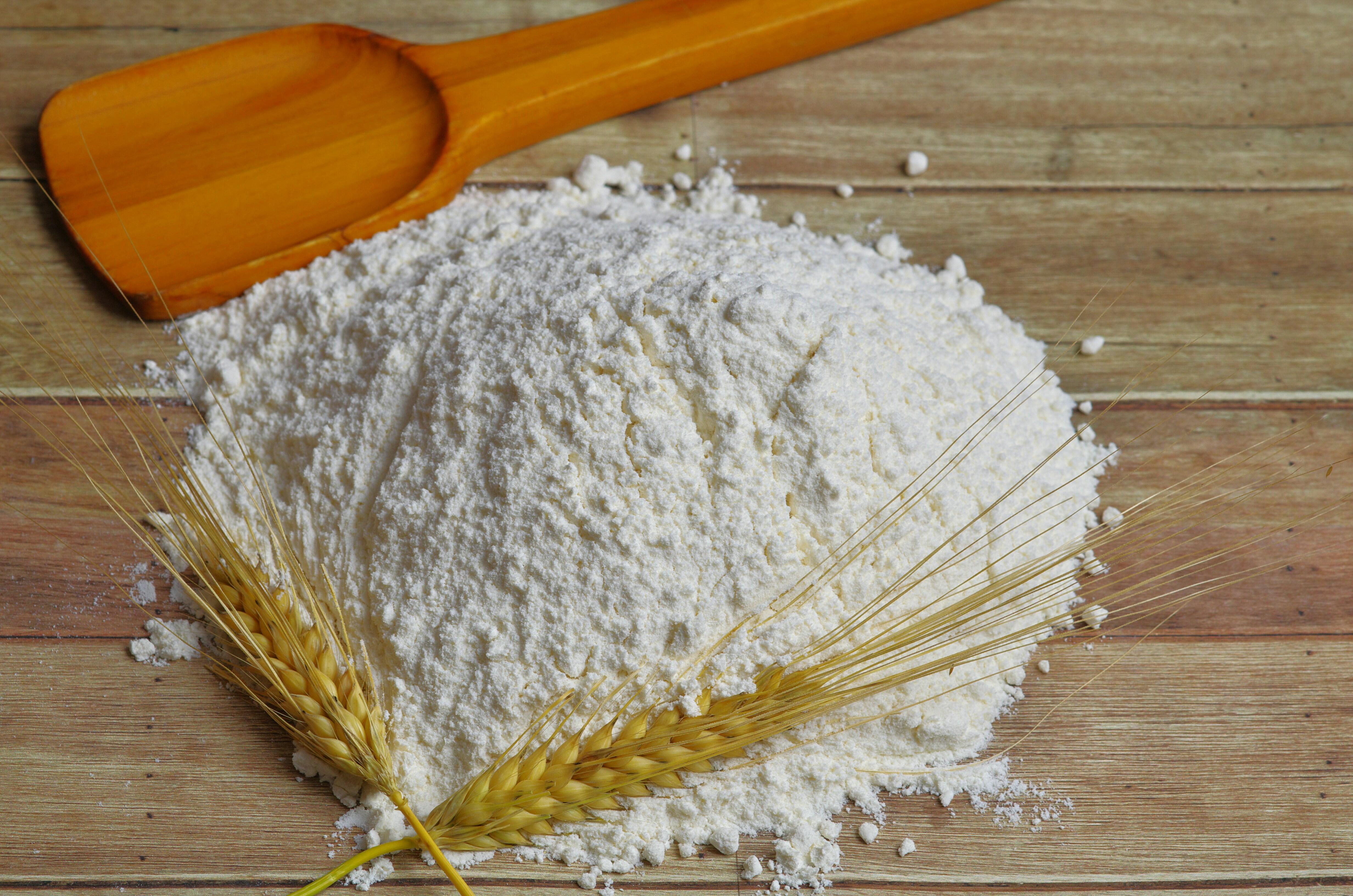 Wheat flour piled on a wooden surface with wheat stalks and a wooden scoop, representing the primary raw ingredient used in ramen noodle production.
