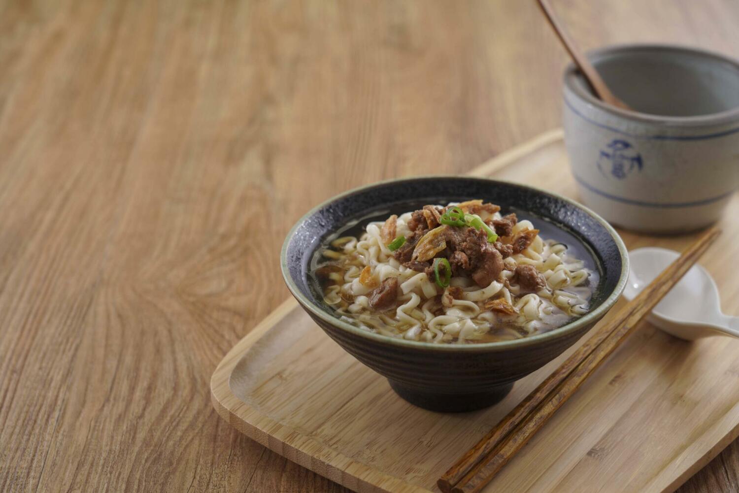 Steam-cooked healthy ramen noodles served in clear broth with braised pork and scallions in a ceramic bowl on a wooden tray.