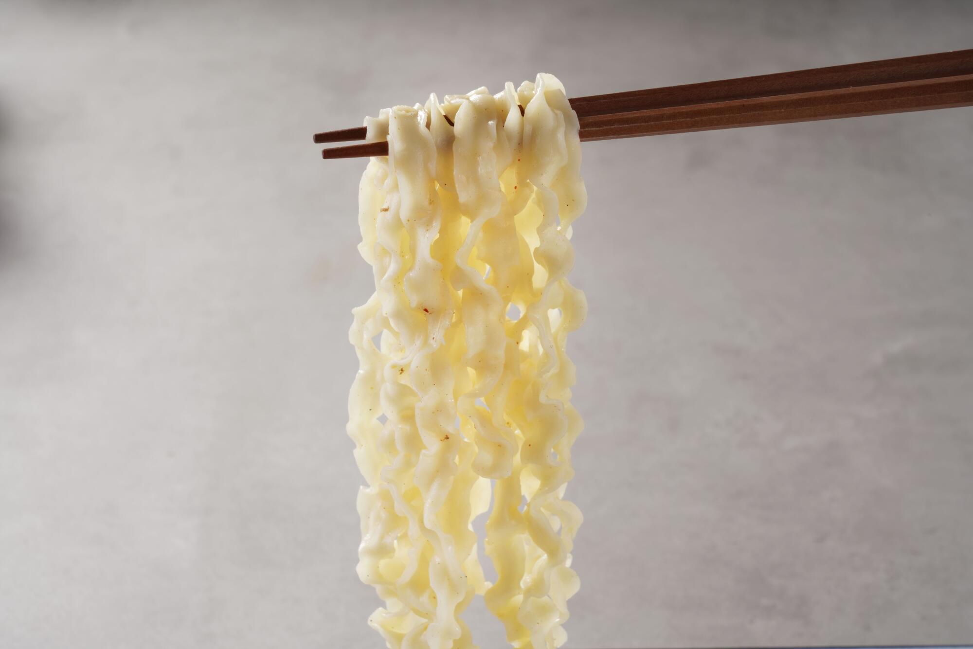 Steam-cooked ramen noodles lifted with chopsticks, showing smooth texture and light, springy elasticity.