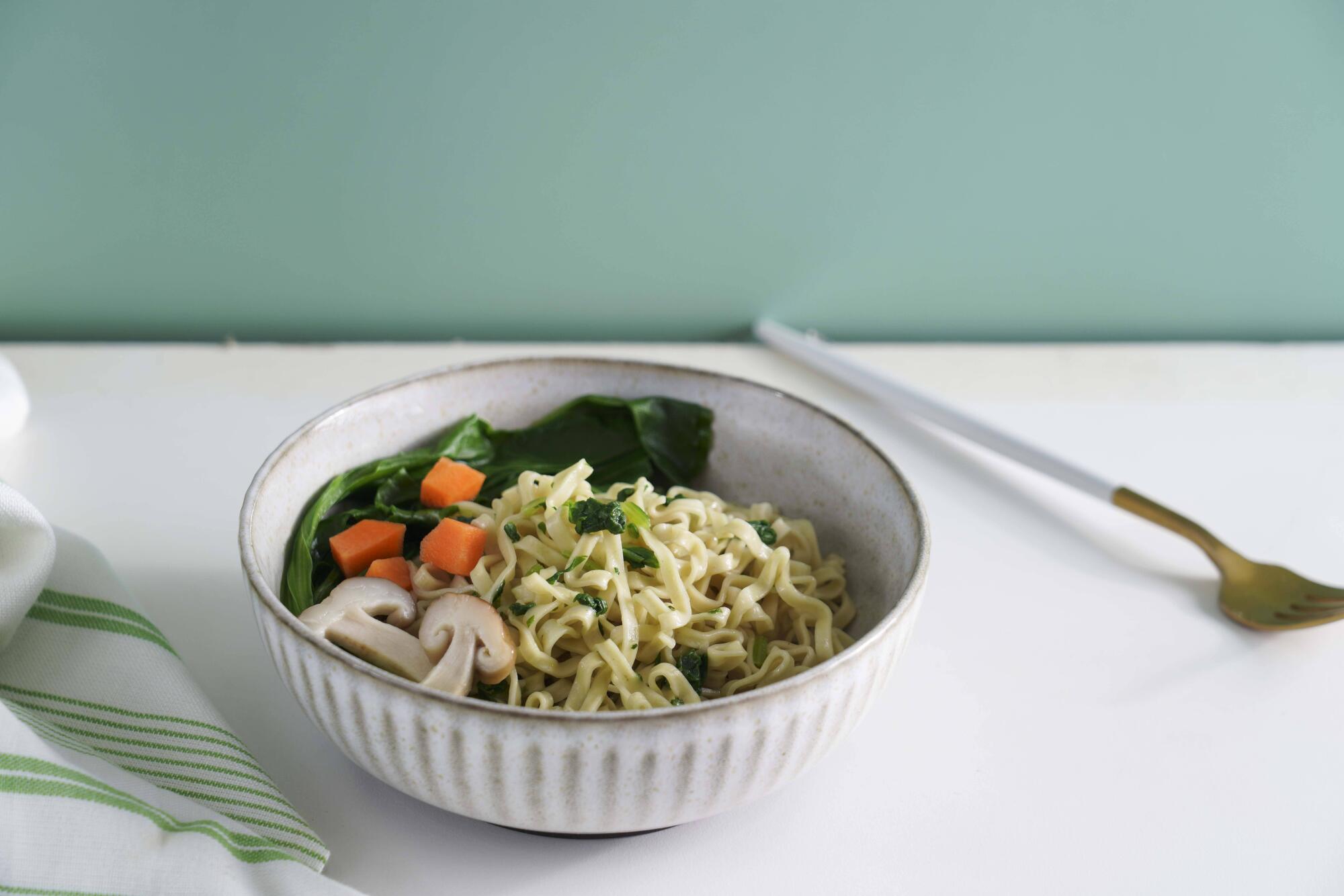 Healthy instant ramen made with steam-cooked noodles, served with mushrooms, carrots, and leafy greens in a light ceramic bowl on a clean tabletop.