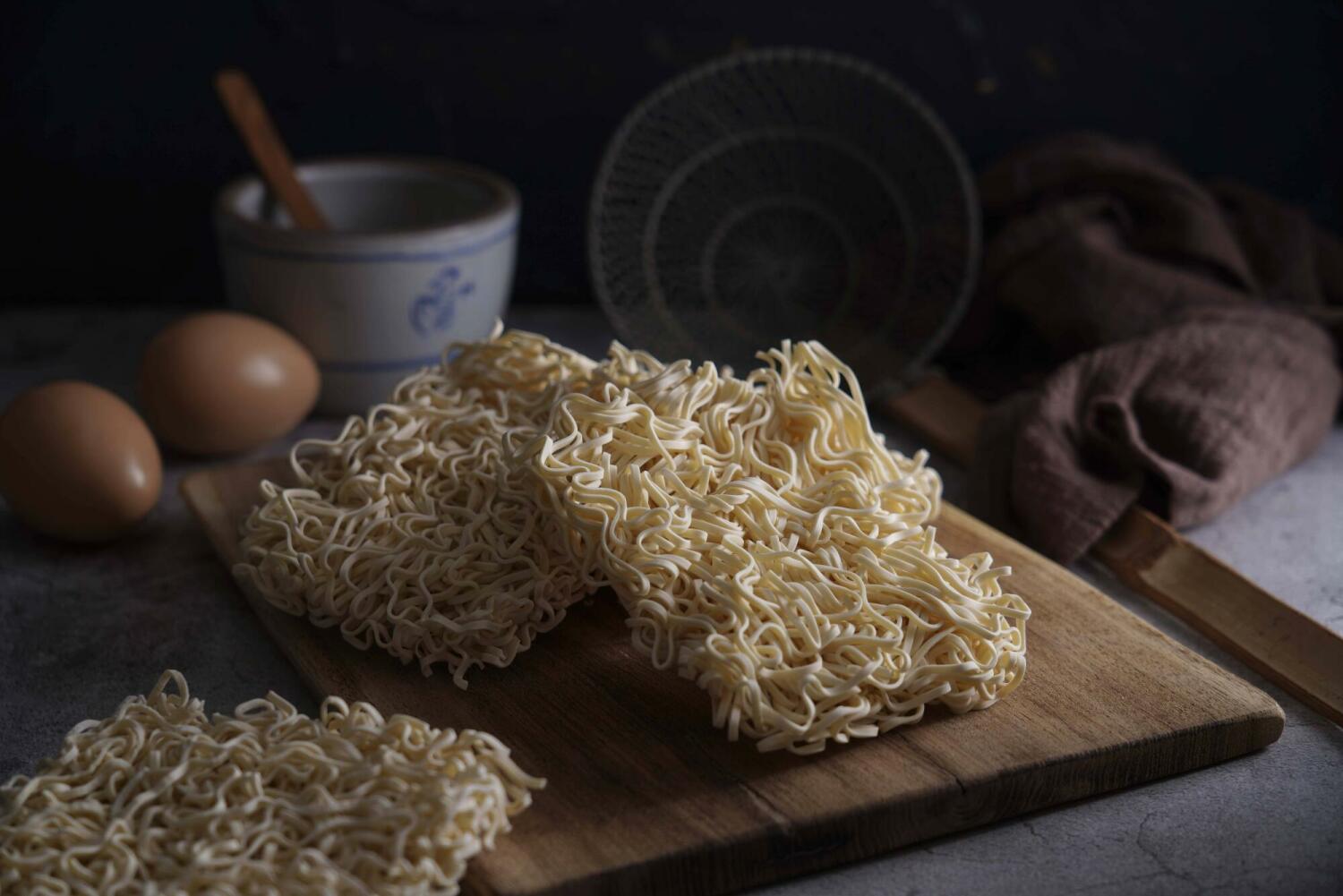 Non-fried steam-cooked ramen sheets stacked neatly on a wooden board, showing clean, dry, oil-free texture.