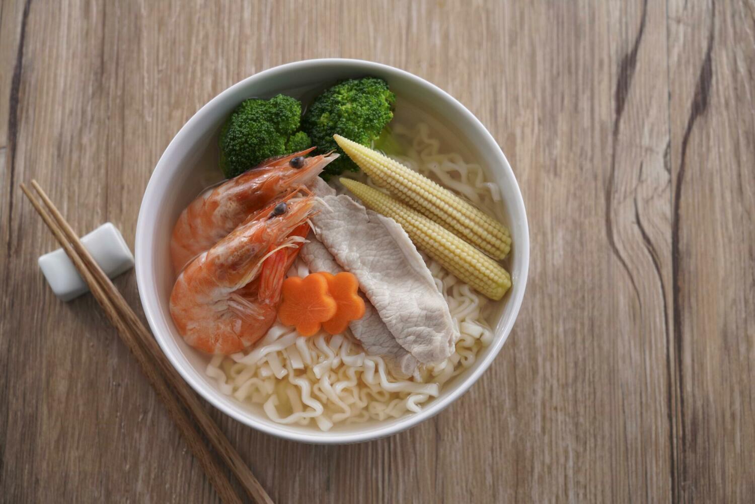 Steam-cooked ramen noodles in clear broth topped with shrimp, pork, baby corn, broccoli, and carrots, showing a balanced and healthy instant ramen meal.