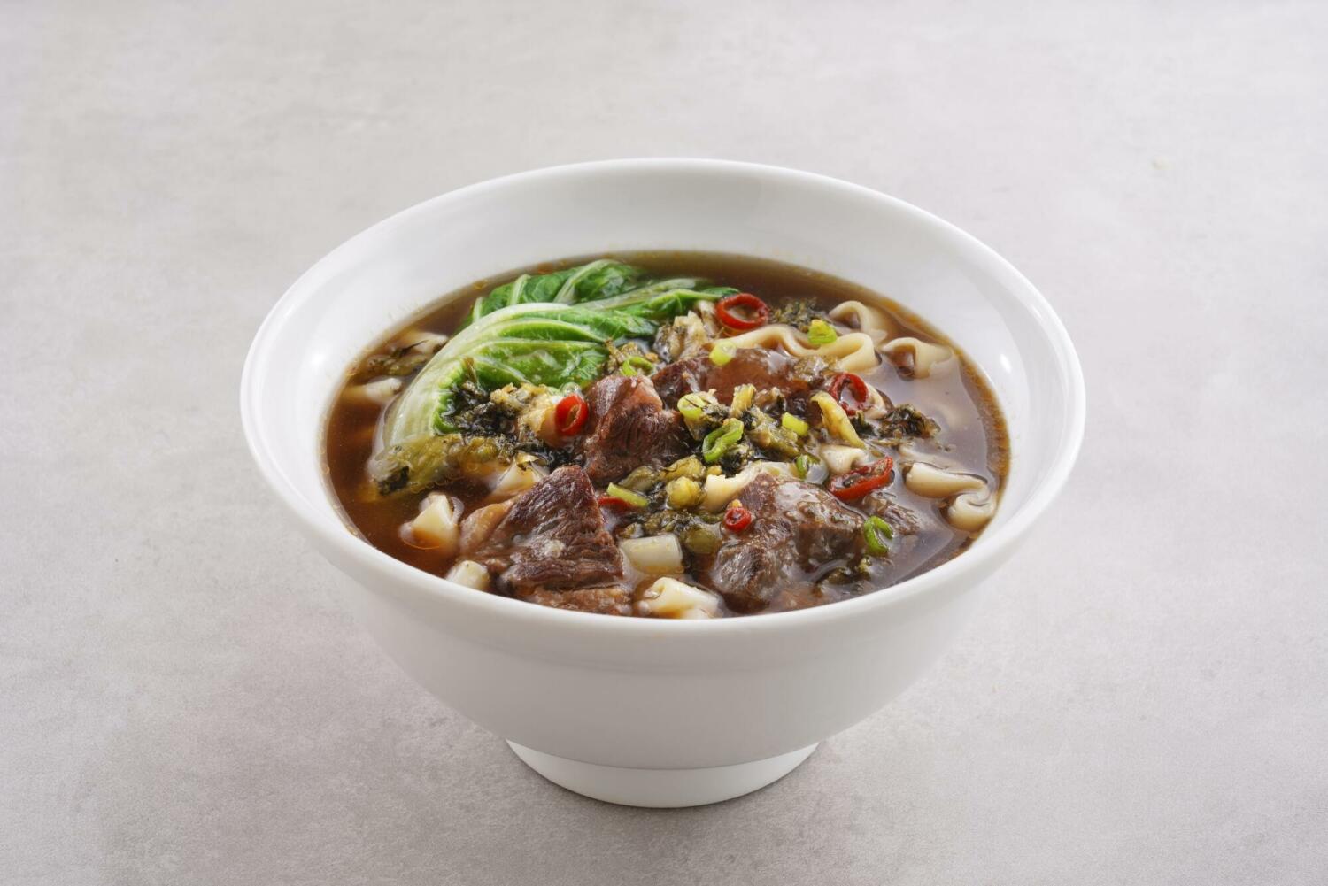 紅燒牛肉麵,搭配刀削麵、大塊牛腱、青江菜、酸菜與辣椒,湯色濃郁,呈現層次分明的紅燒牛肉麵風味。