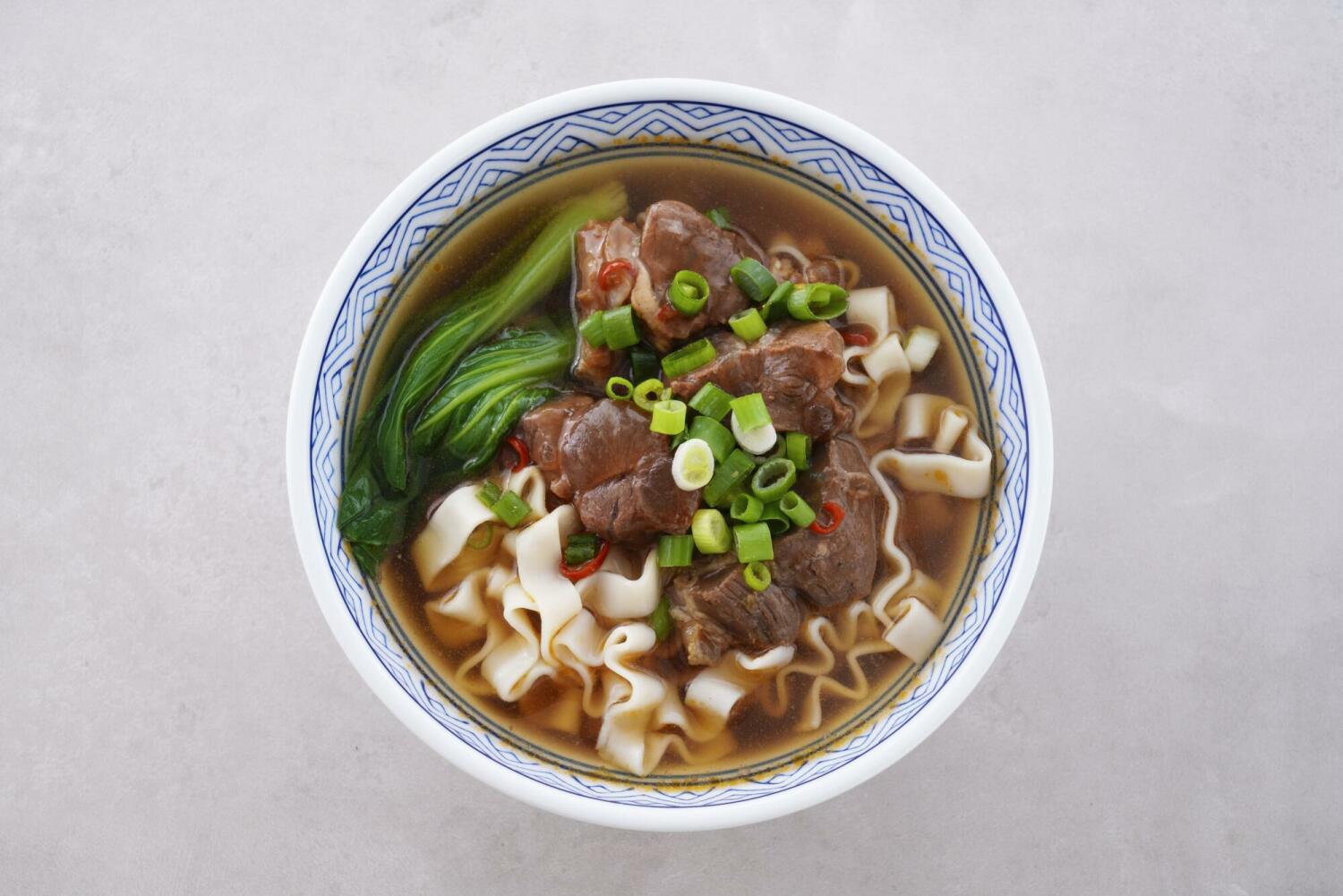 一碗紅燒牛肉麵,搭配刀削麵、大塊牛腱、青江菜與蔥花,湯色濃郁,呈現經典台式風味。