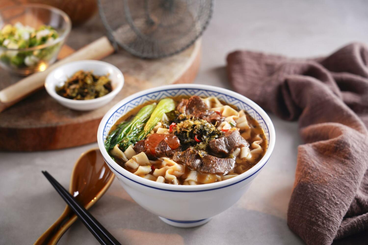 Bowl of SING-LIN FOODS beef flavored ramen topped with beef, bok choy, and pickled mustard greens.
