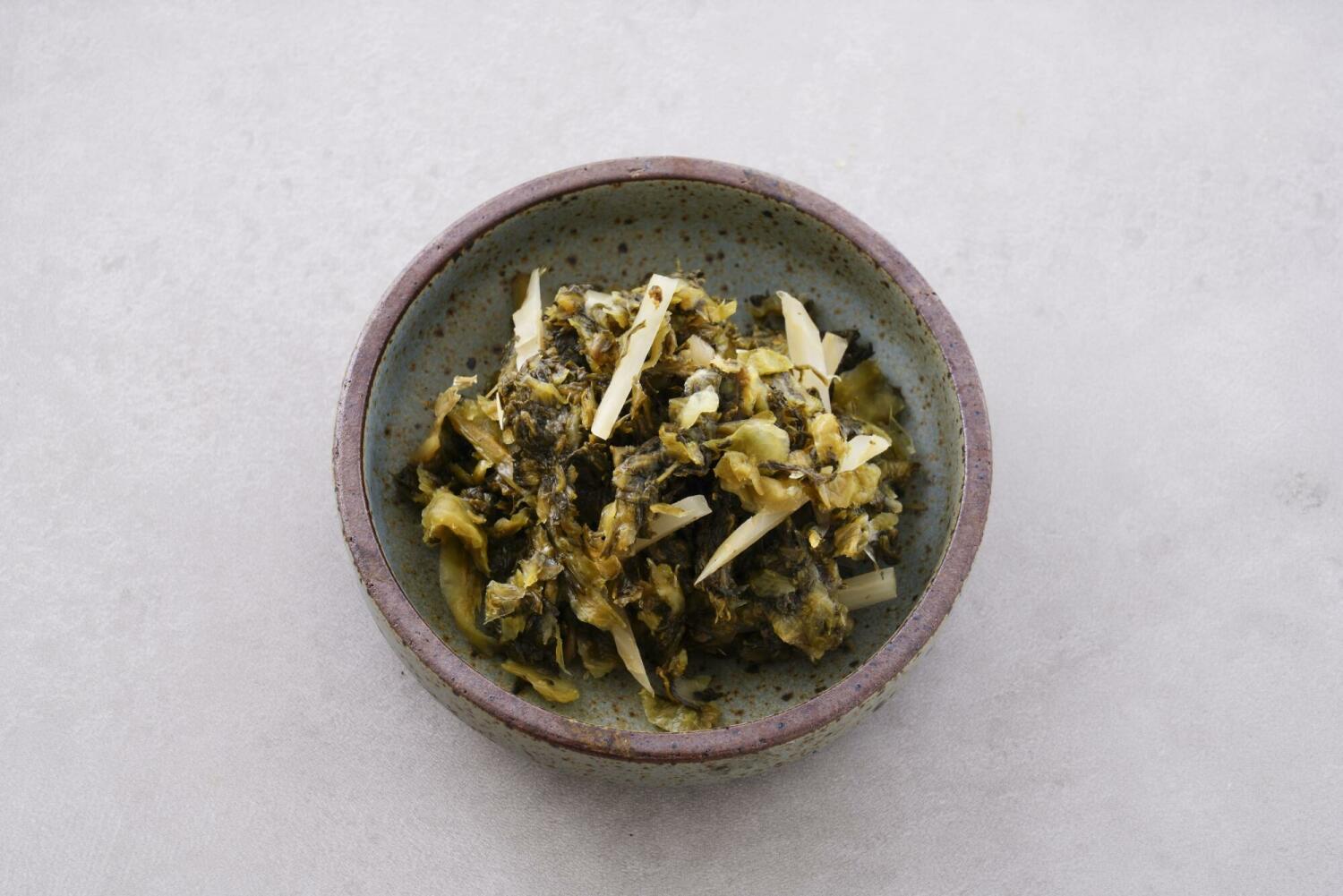 Taiwanese pickled mustard greens (suancai) served in a small bowl, a classic topping for beef noodle soup.