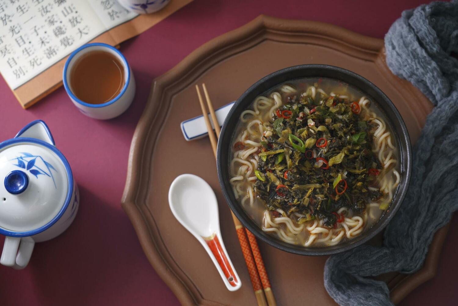 A cozy bowl of beef flavored ramen with pickled mustard greens, surrounded by tea, chopsticks, and warm Taiwanese décor.