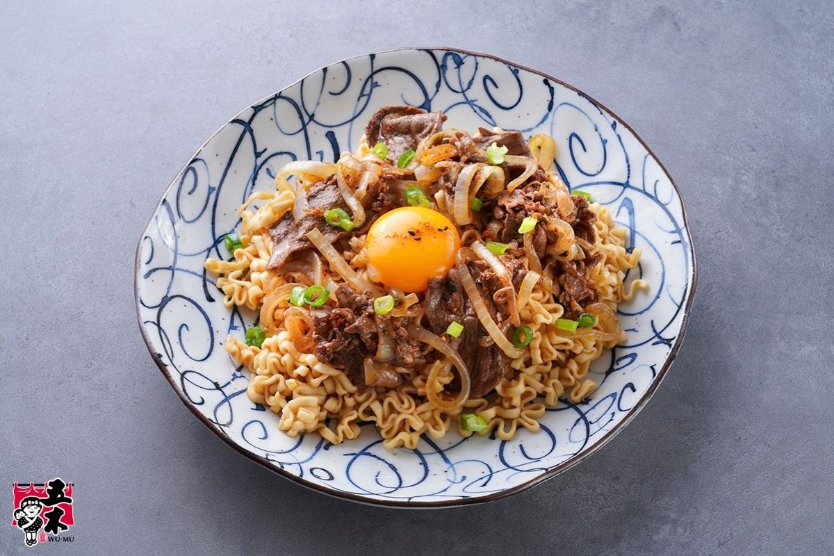Black pepper beef noodles topped with sliced beef, onions, chopped scallions, and an egg yolk.