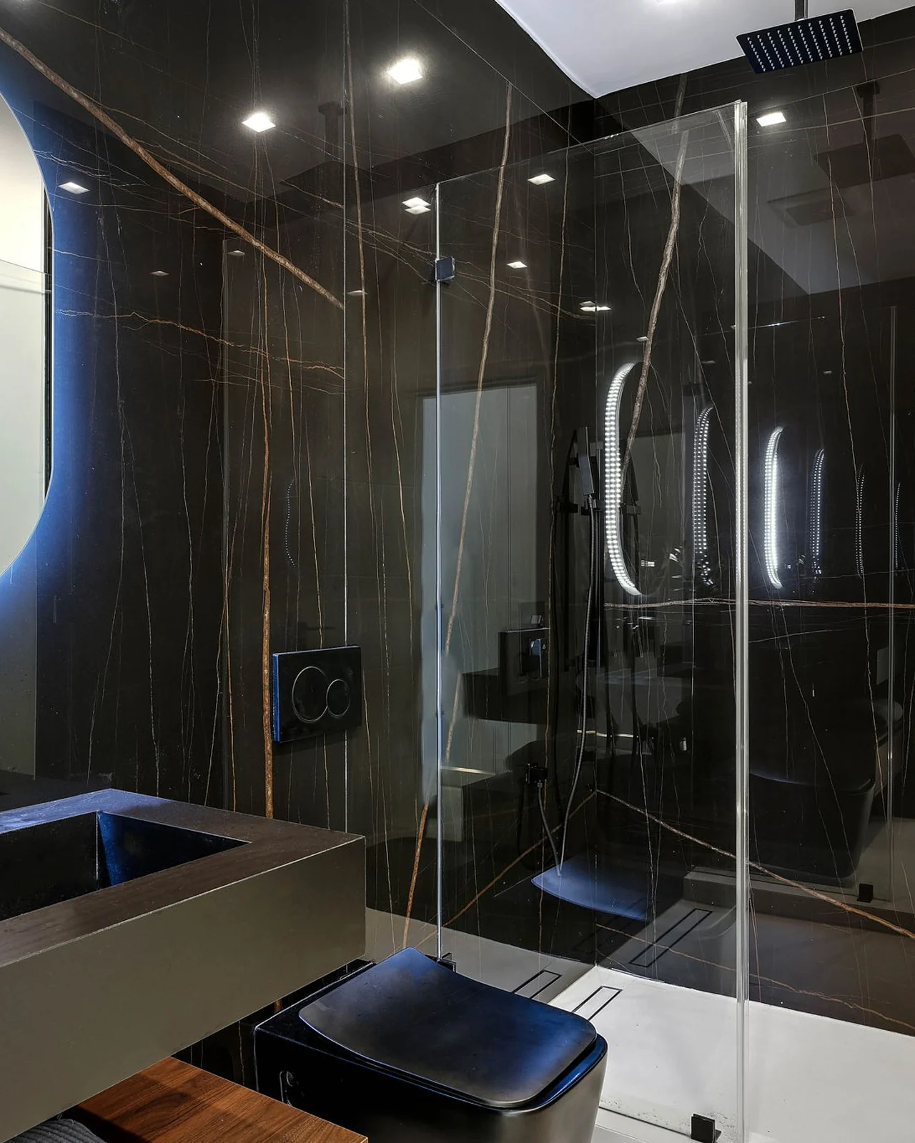 The replacement bathroom in dark stone floor to ceiling, a glass screen with no frame, and a tub set clear of the walls