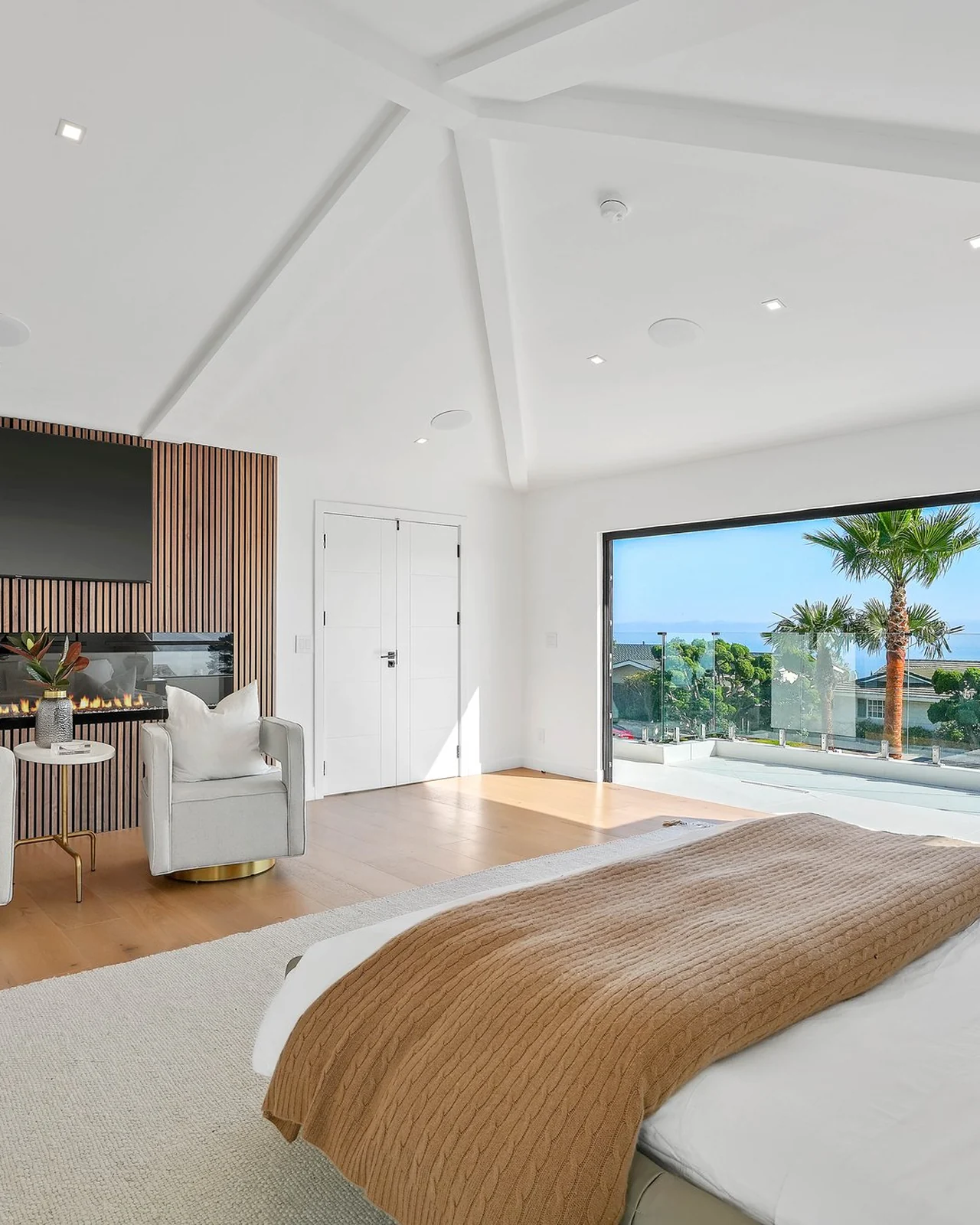 The rebuilt suite — a wall of vertical timber battens behind the bed, oak boards underfoot, chairs set off to one side, glazing straight out to the water
